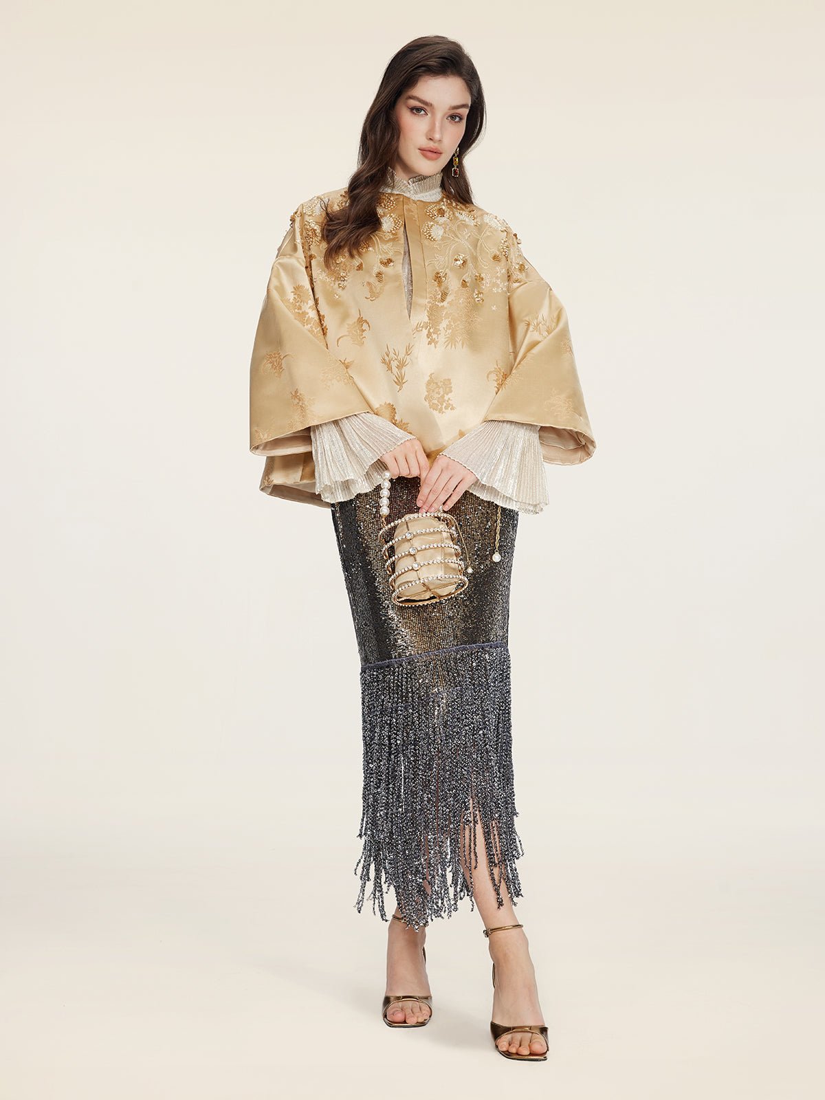 A woman wears the Social Queen 100% Silk Floral Embroidered Satin Jacket, styled with a metallic silver fringe skirt, heeled sandals, and a small embellished handbag against a plain background.