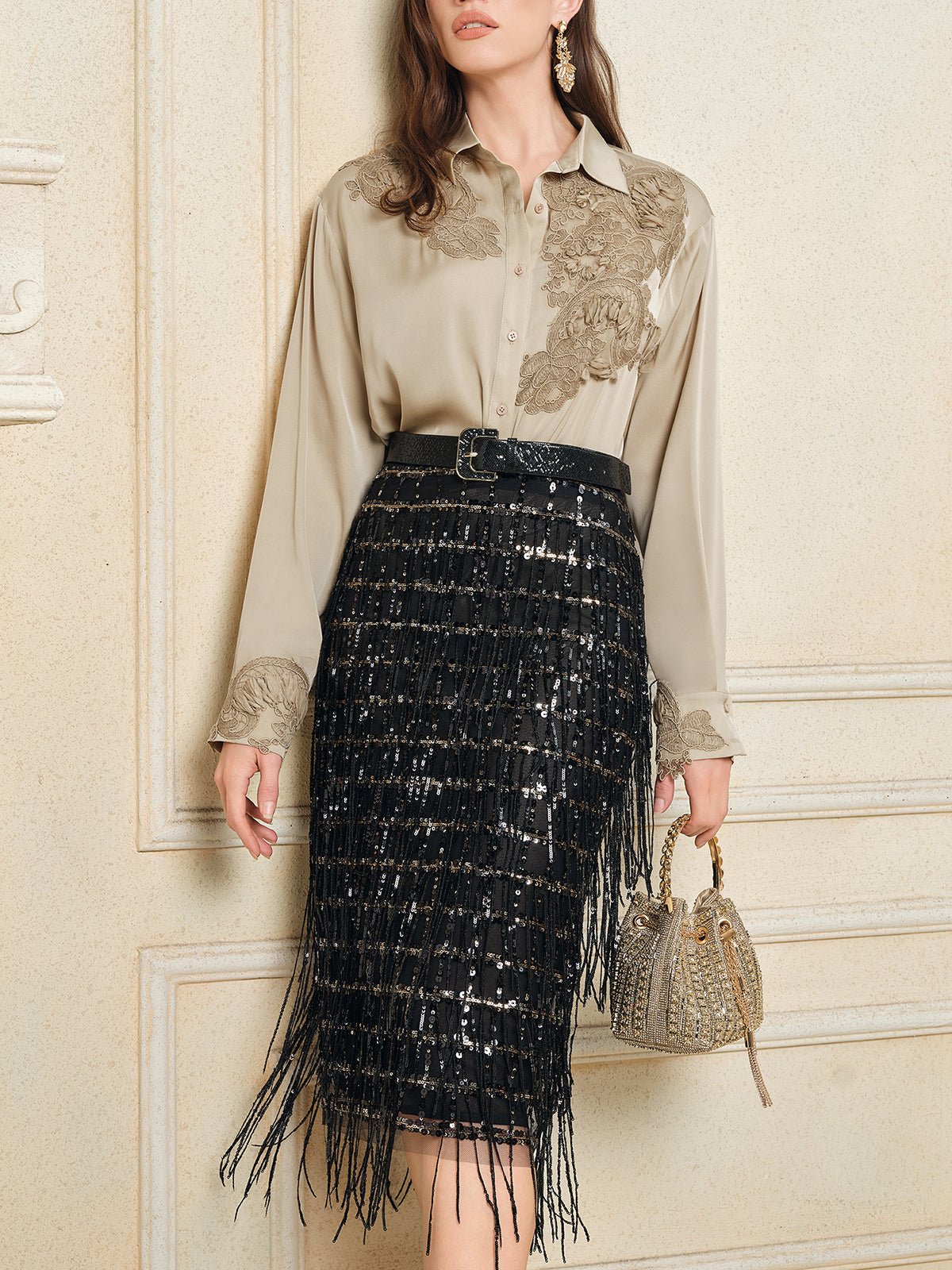 A woman wears the Social Queen 100% Silk Retro Floral Appliqué Satin Blouse, tucked into a black sequined fringe skirt, holding a beaded handbag while standing against a cream-colored wall.
