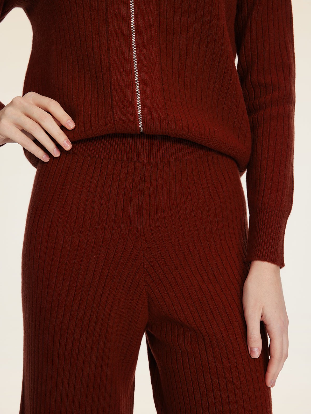 A person wears Social Queen's 100% Wool Knit Elastic Trousers in maroon, featuring a straight-leg silhouette and elastic waist, paired with a matching ribbed sweater. One hand rests on their waist, the other by their side.