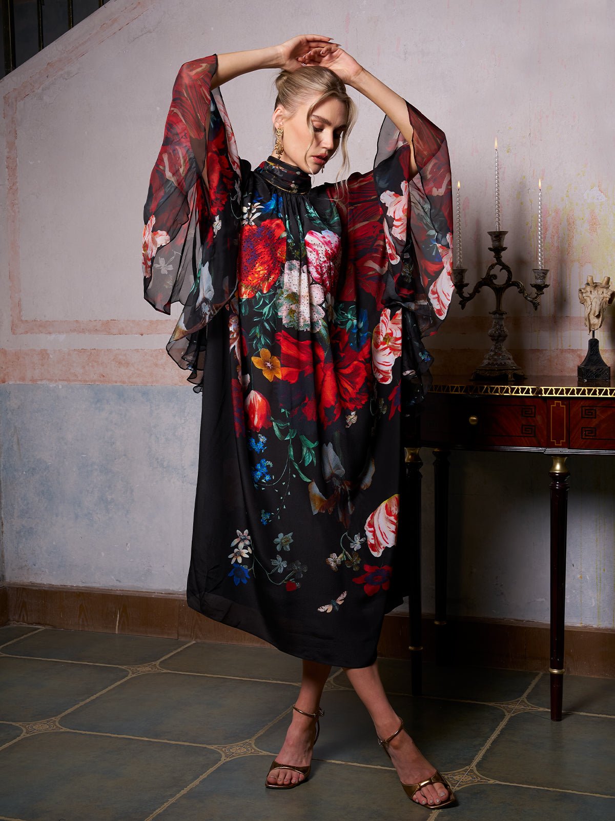 A woman poses indoors near a dark wooden table in the Social Queen Artistic Floral Print Ruffle Dress, featuring sheer wide sleeves—a stunning choice for wedding guests.