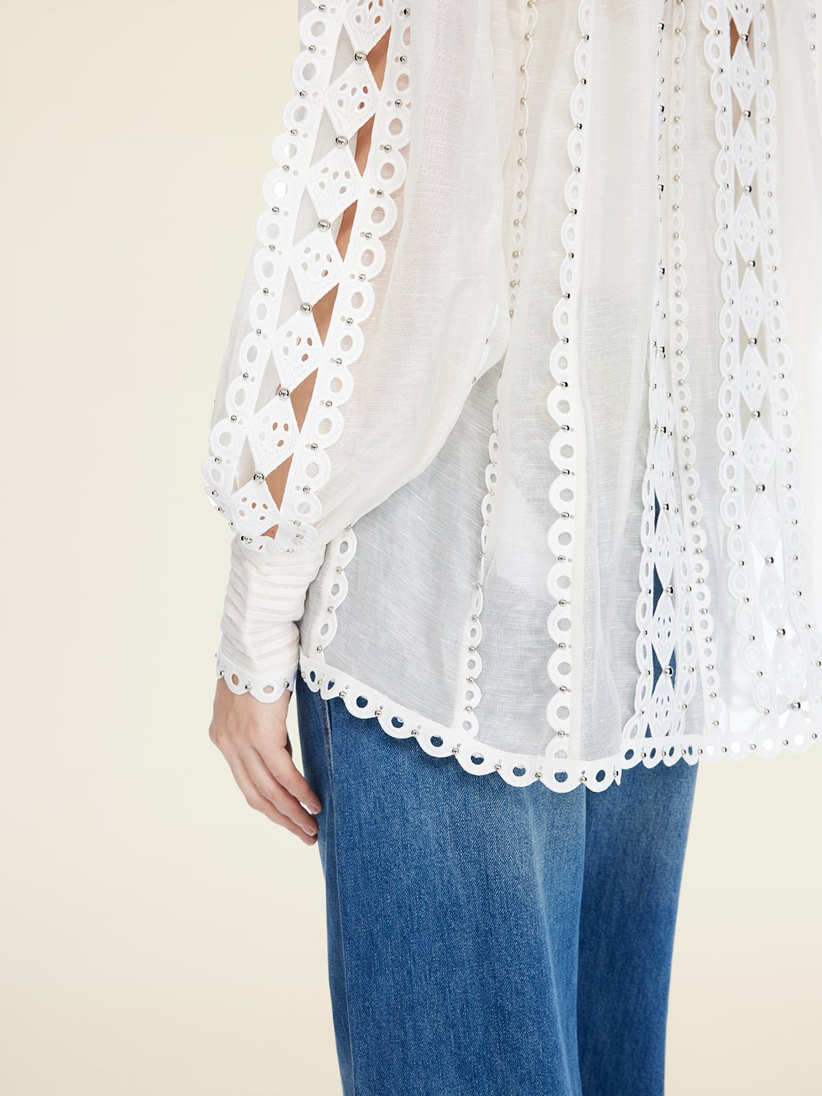 A person wearing Social Queen's Beaded Geometric Lace Blouse—featuring eyelet lace details, sheer fabric, and lantern sleeves—with blue jeans, shown from mid-torso to thigh.