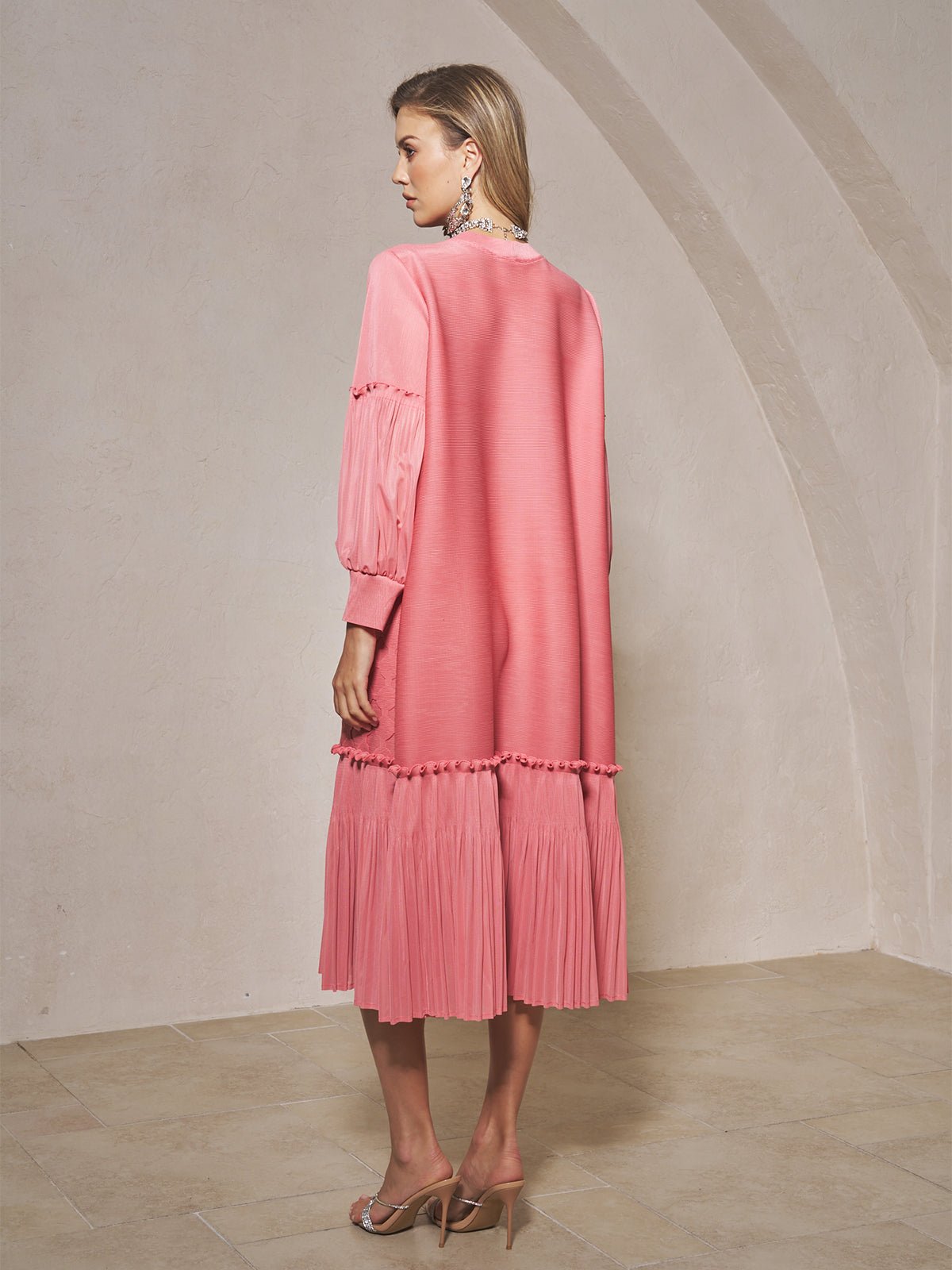 A woman stands indoors, facing away, wearing the Social Queen Beaded Jacquard Pleated Midi Dress paired with heeled sandals.