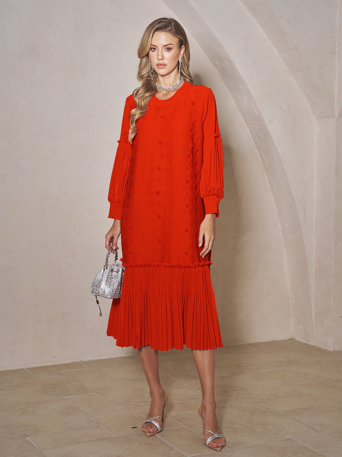 A woman stands indoors wearing the Social Queen Beaded Jacquard Pleated Midi Dress in red, styled with silver sandals, a silver necklace, and a small silver handbag.