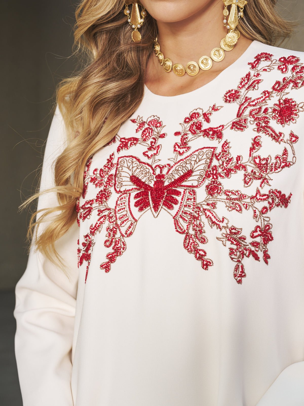A woman wears the Social Queen Butterfly Embroidered A-Line Dress, a white matte satin piece with red and gold floral and butterfly embroidery, styled with gold earrings and a necklace—ideal for attending weddings.