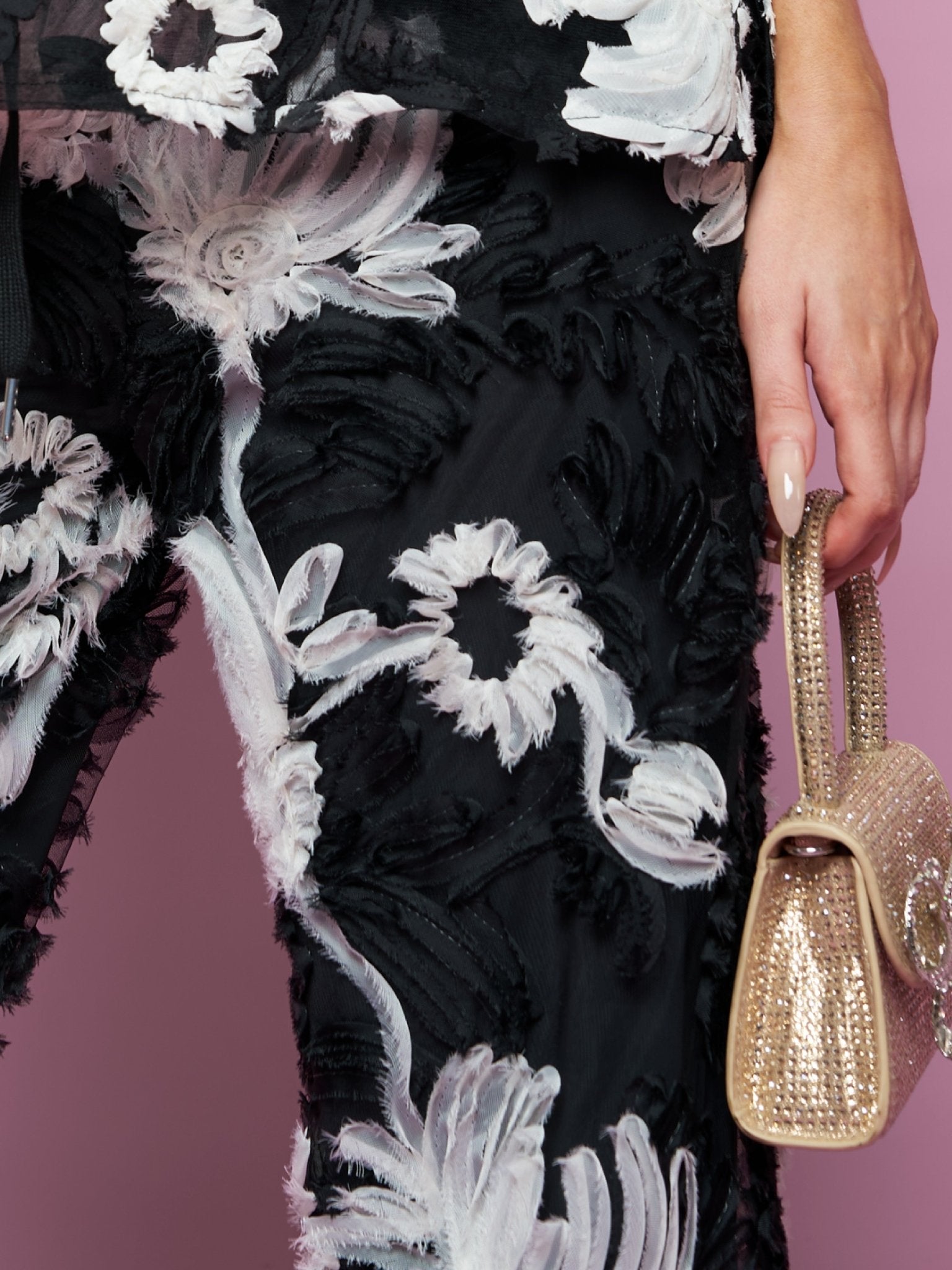A model in Social Queen's Contrast Floral Sheer Wide-Leg Pants holds a small gold textured handbag, set against a pink background.