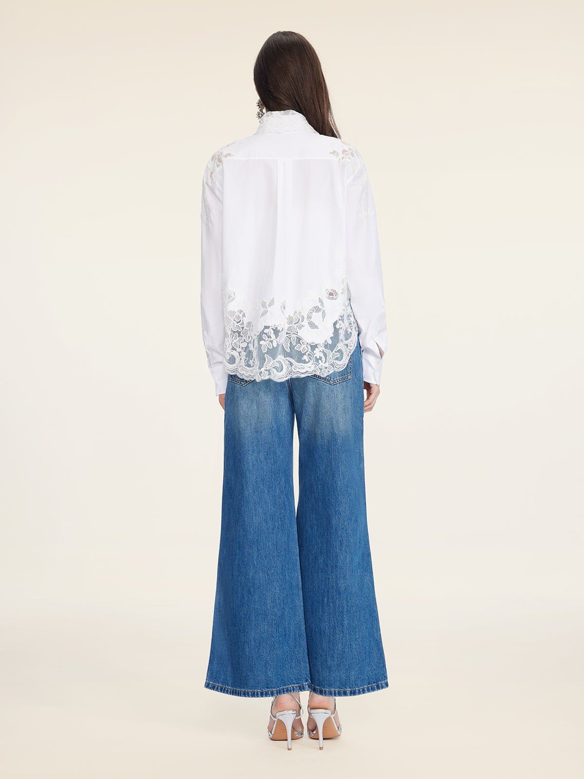 A person with long hair, seen from behind, wears the Social Queen Cropped Embroidered Lace Panel Blouse, paired with wide-leg blue jeans and white heeled sandals, standing against a plain background.