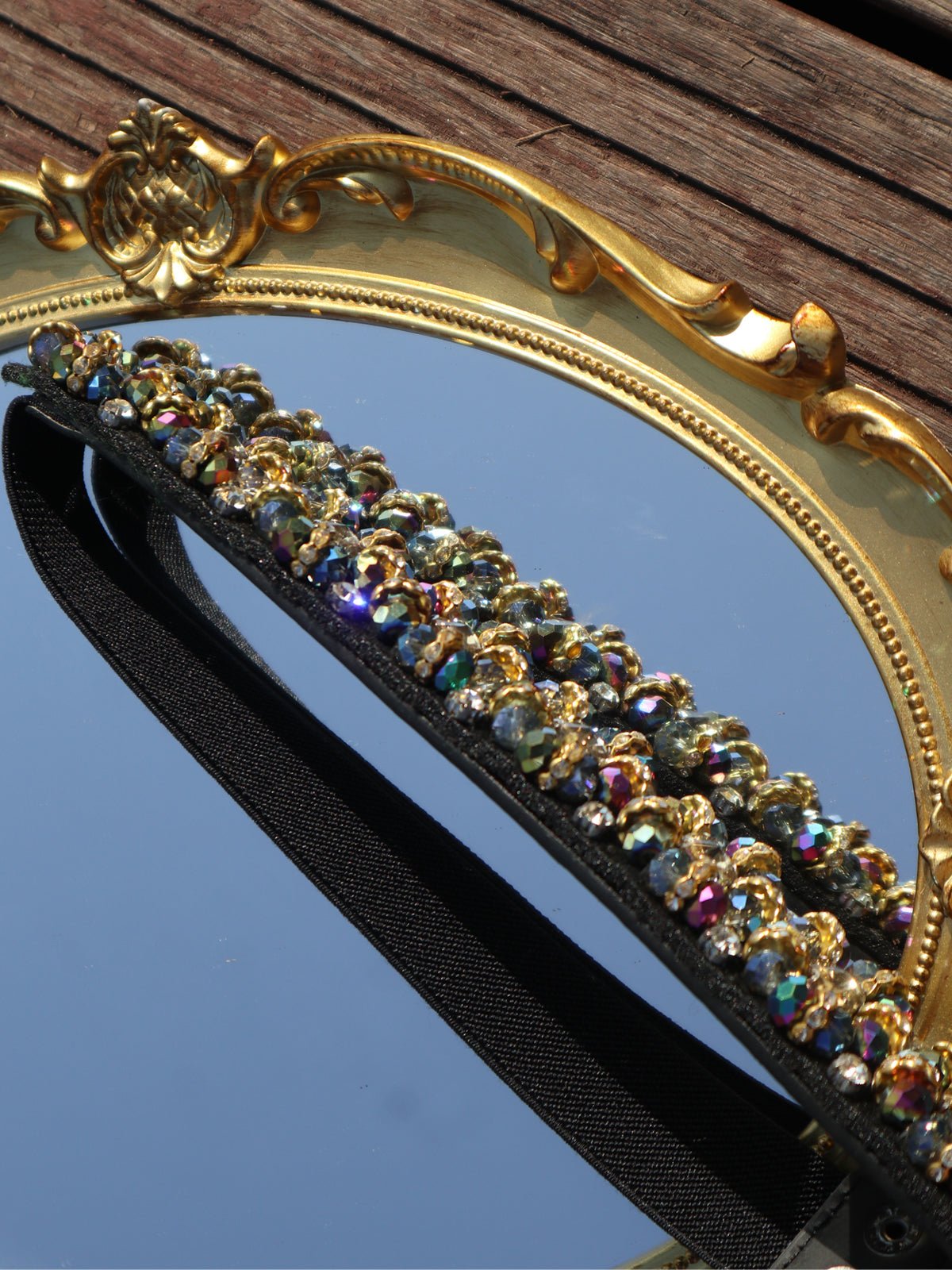 The Crystal-Embellished Vintage Belt by Social Queen lies atop an ornate gold mirror, reflecting sky and wood—an elegant, chic accessory perfect for elevating any wedding guest ensemble.