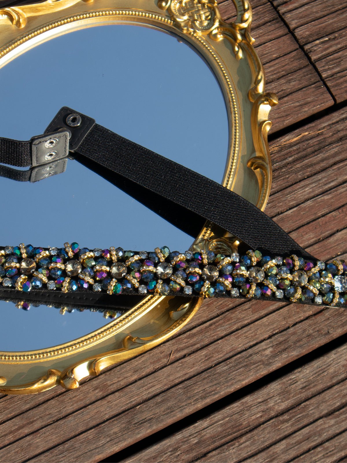 The Social Queen Crystal-Embellished Vintage Belt, featuring multicolored stones and an adjustable buckle, rests on a gold-framed mirror atop wood—an ideal accessory for wedding guests.
