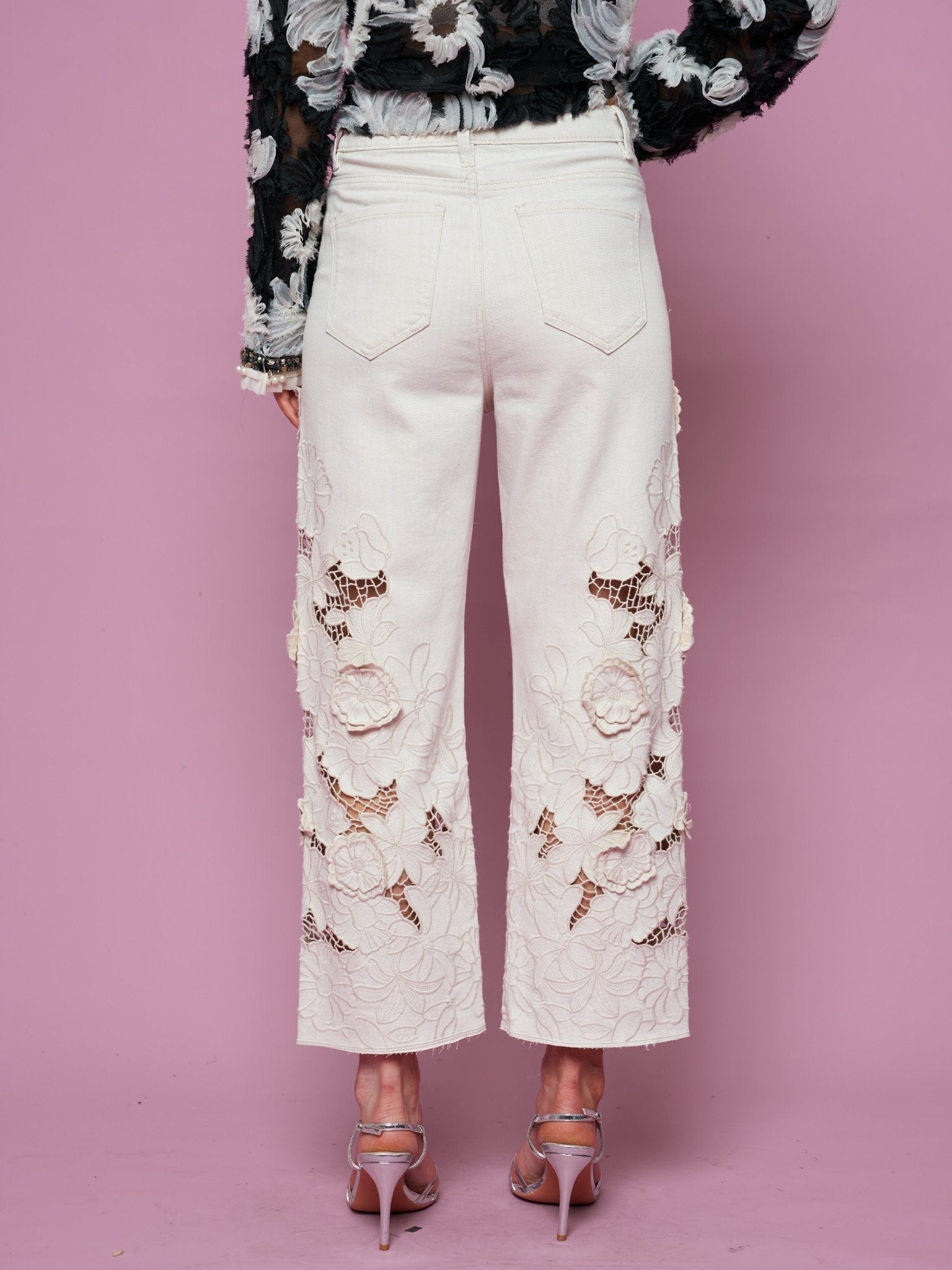 Model wears Social Queen Floral Cutout High-Rise Jean in white and a black floral top, standing against a pink background, shown from the back.