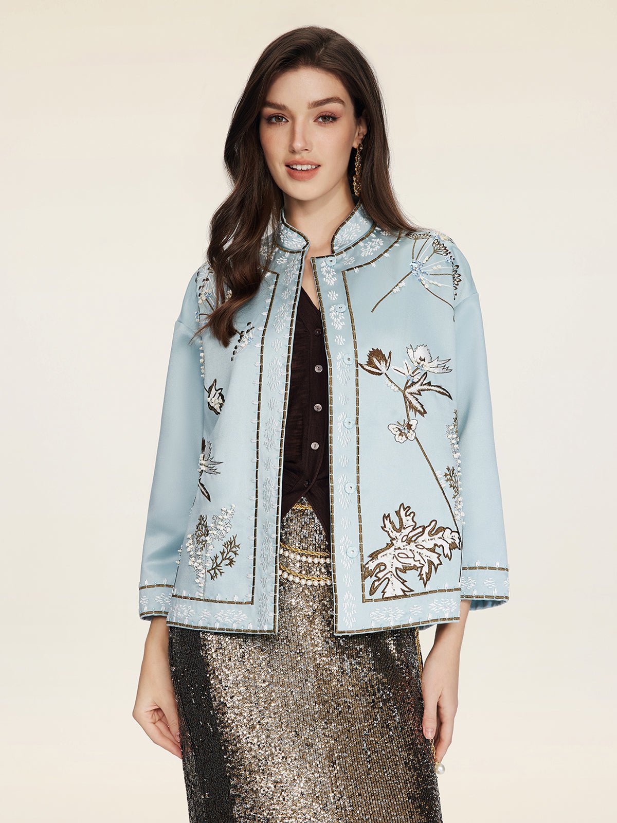 A woman faces forward in a Social Queen Floral Embroidered Beaded Jacket, featuring hand-embroidered florals, over a black top and gold sequined skirt, set against a plain background.