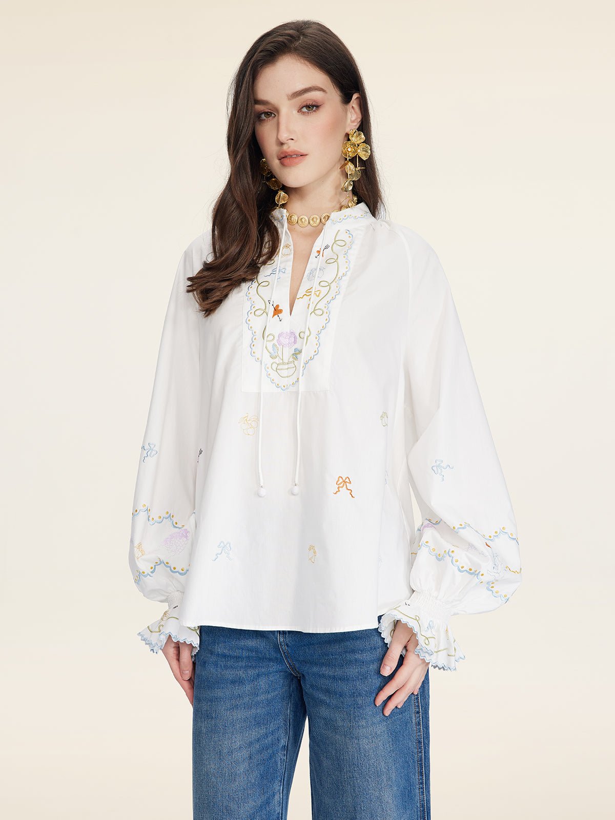 A woman wears the Social Queen Floral Embroidered Cotton Blouse with a relaxed fit and tie neckline, paired with blue jeans, standing against a plain light background.