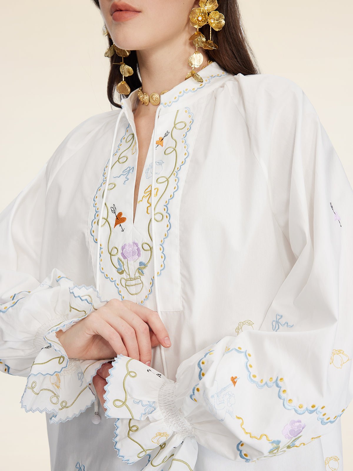 A woman wears the Social Queen Floral Embroidered Cotton Blouse with ruffled cuffs, paired with large gold earrings and a choker necklace.