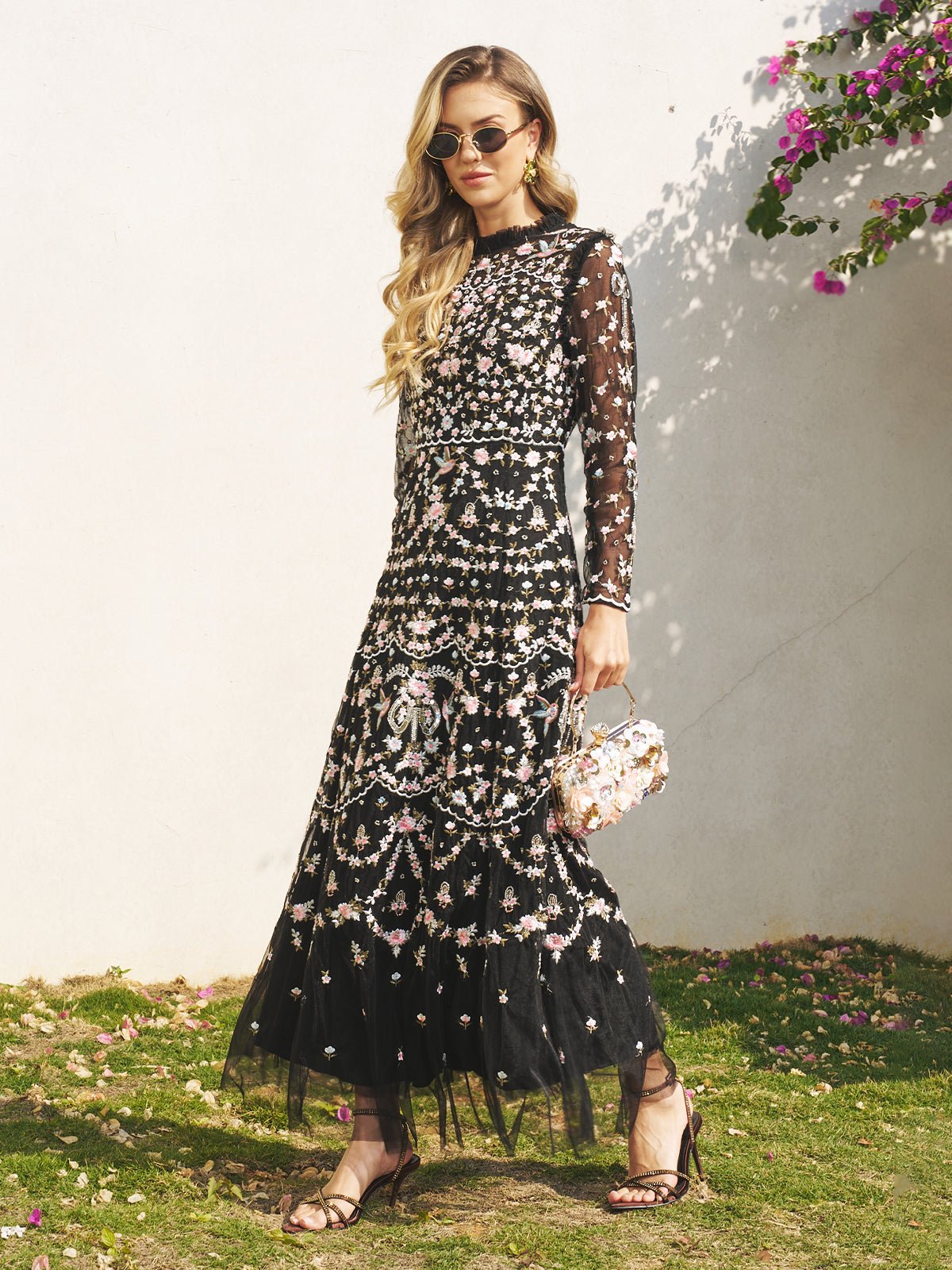 Wearing the Social Queen Floral Embroidered Mesh Dress with sheer tulle panels, sunglasses, and sandals, she stands outdoors holding a floral handbag—a stunning wedding guest look.