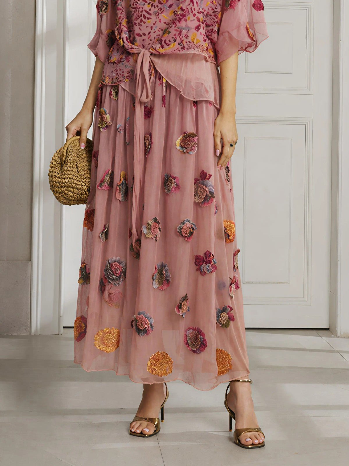 A person wears the Social Queen Floral Embroidered Silk A-Line Skirt, holding a woven bag and standing in sandals before a white door.