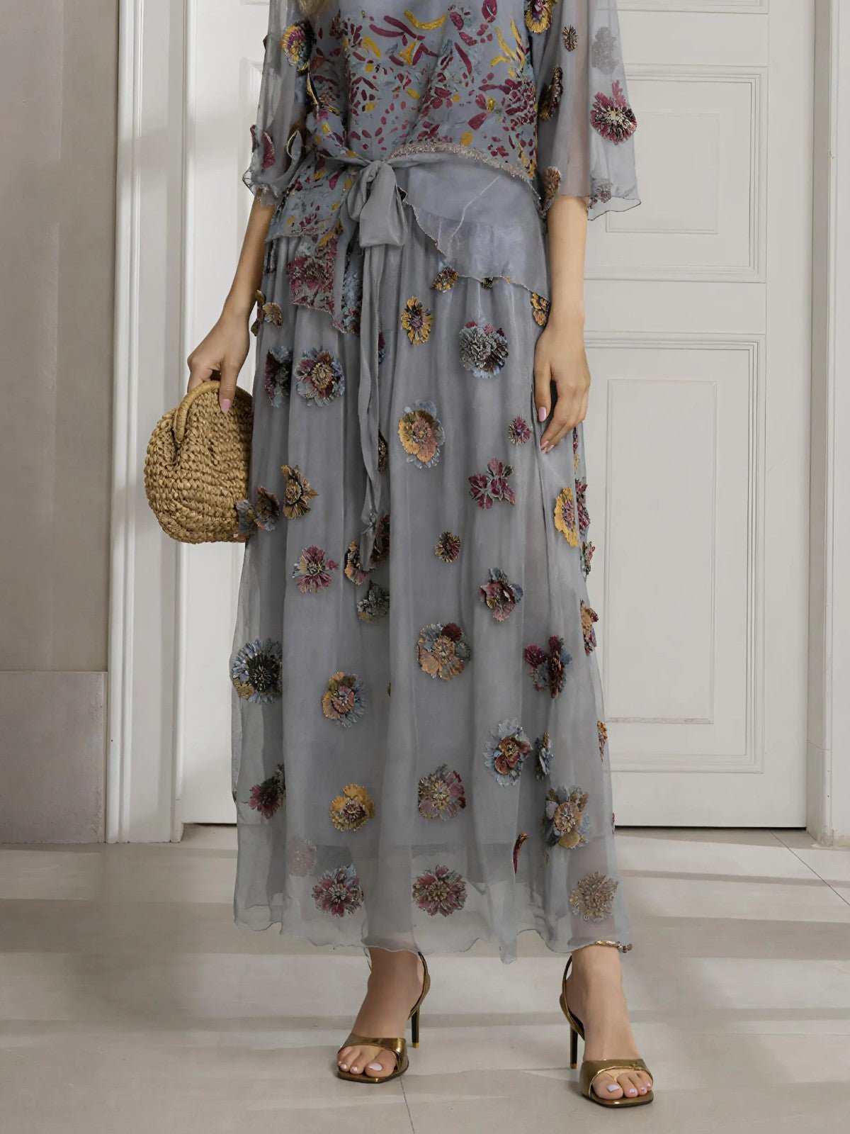 A person in a Social Queen Floral Embroidered Silk A-Line Skirt stands by a white door, pairing the skirt with open-toe heels and a small straw handbag.