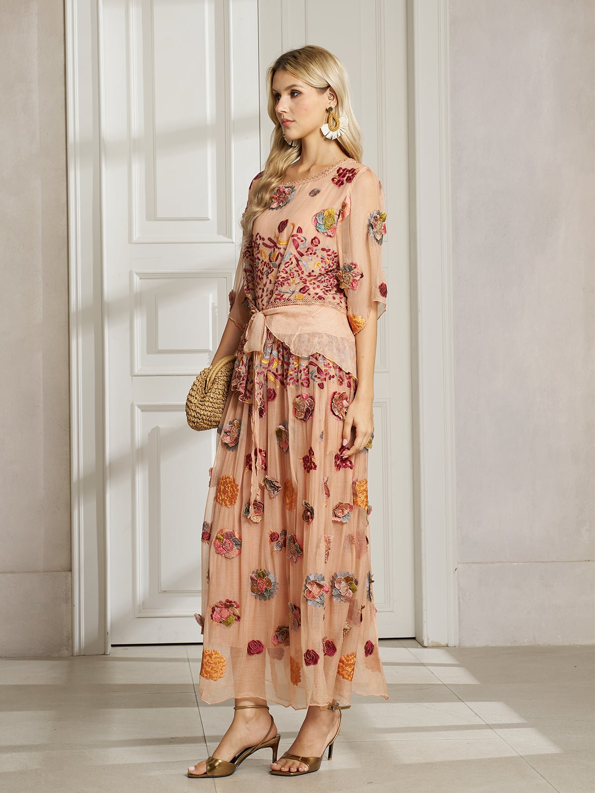 A woman stands indoors wearing the Social Queen Floral Embroidered Silk A-Line Skirt, paired with a woven handbag and gold open-toed heels.