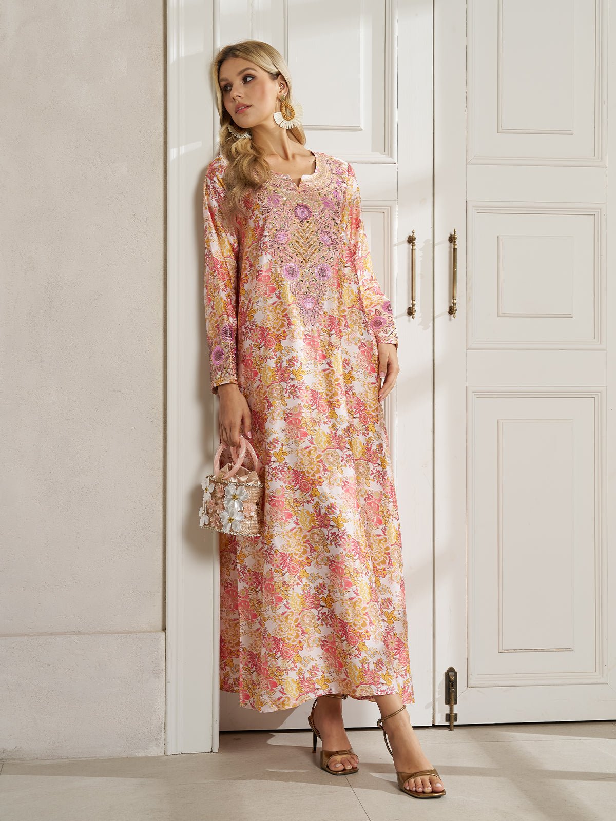 A woman stands indoors wearing the Social Queen Floral Print Beaded Dress with long sleeves, styled with heeled sandals, a small handbag, and gold earrings.