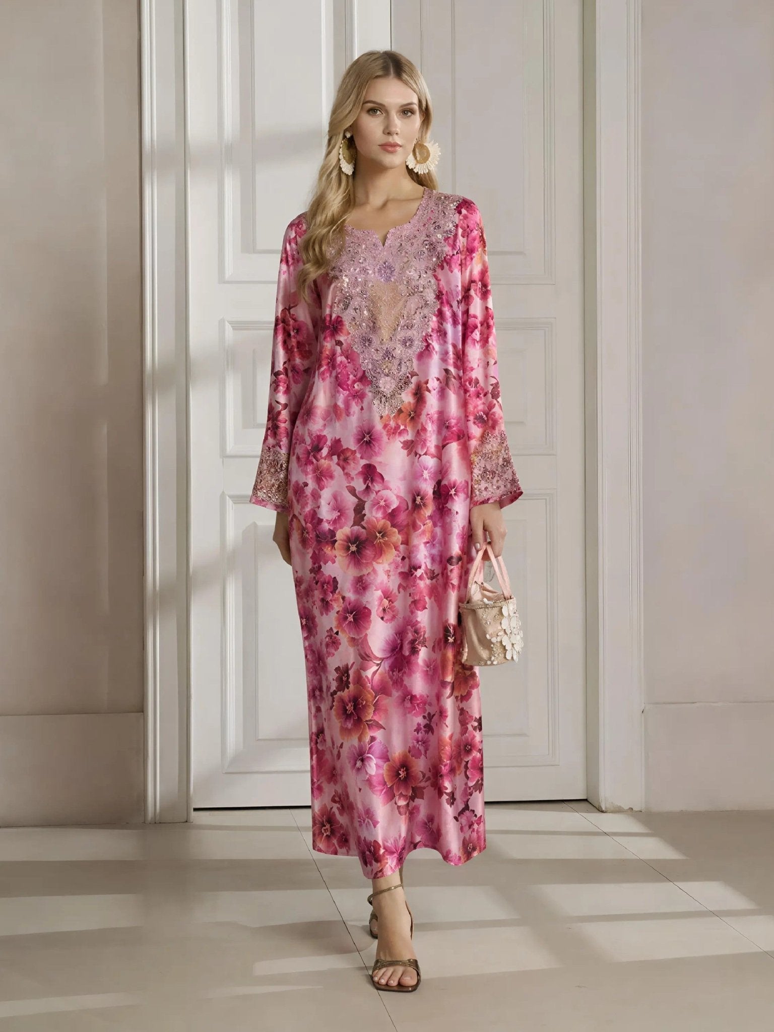 A woman stands indoors in the Social Queen Floral Print Beaded Dress, featuring a long silhouette with a botanical pattern and delicate beadwork, paired with a small handbag and heeled sandals.