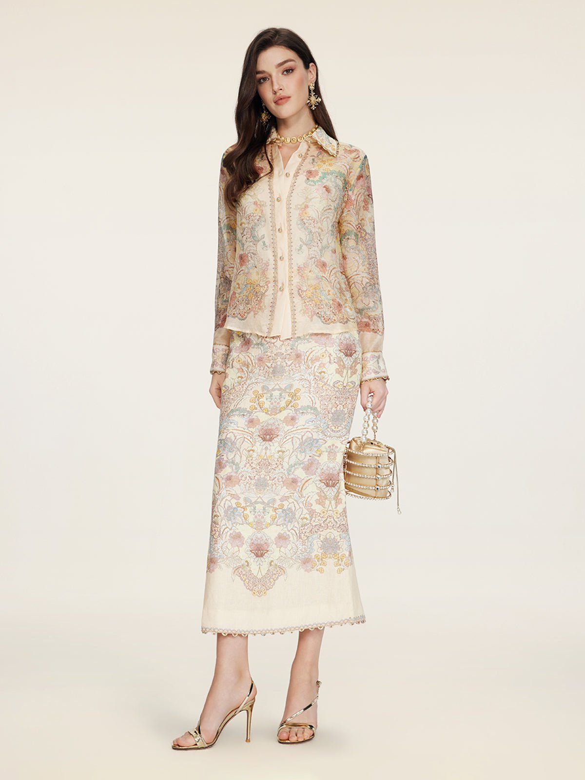 A woman wears the Social Queen Floral Print Collared Blouse with a matching skirt, gold high-heeled sandals, and a small gold handbag, standing against a plain light background.
