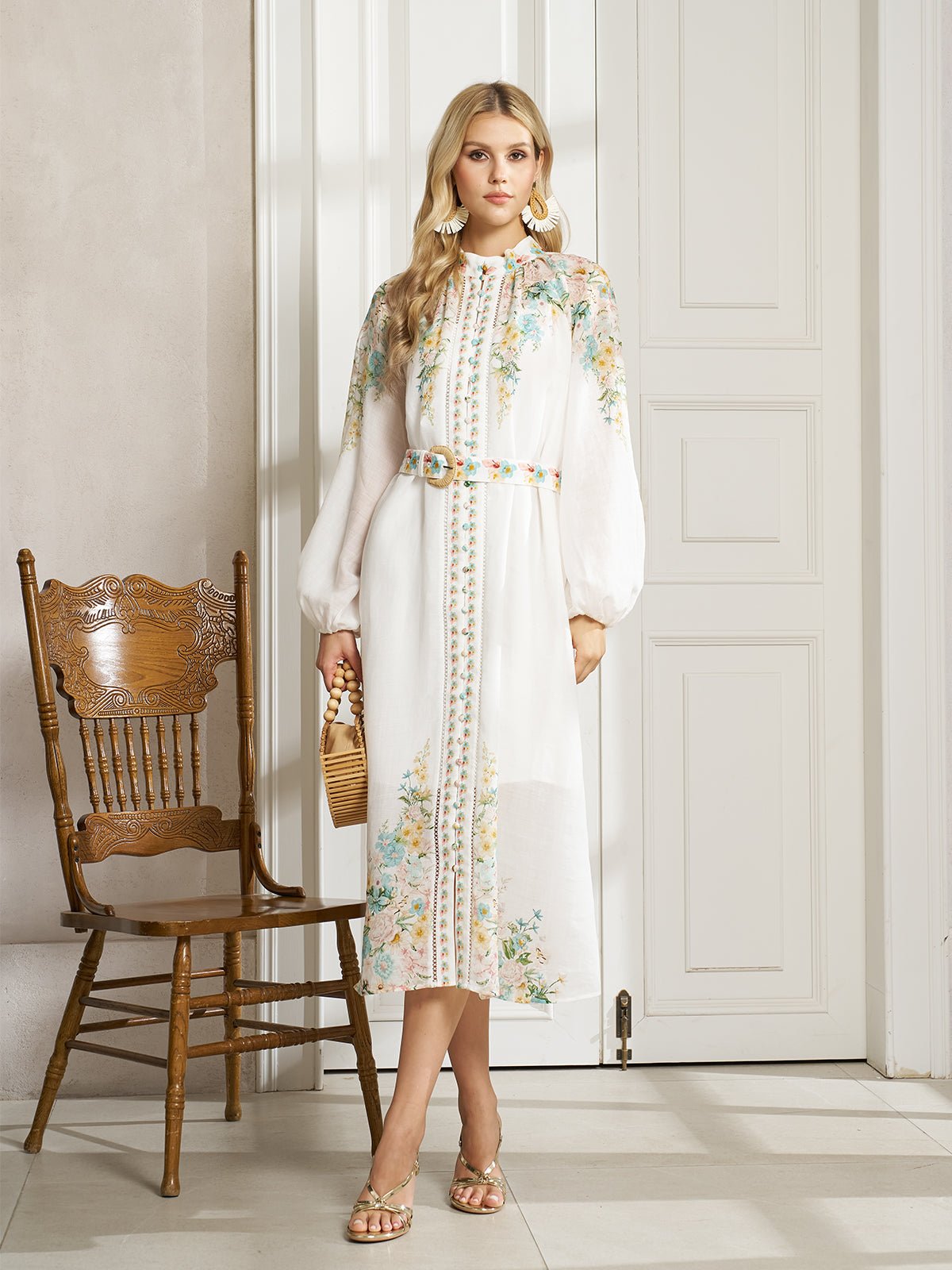 A woman stands indoors by a wooden chair in the Social Queen Floral Printed Stand-Collar Dress, holding a wicker handbag and wearing sandals—the perfect go-to spring vacation outfit.