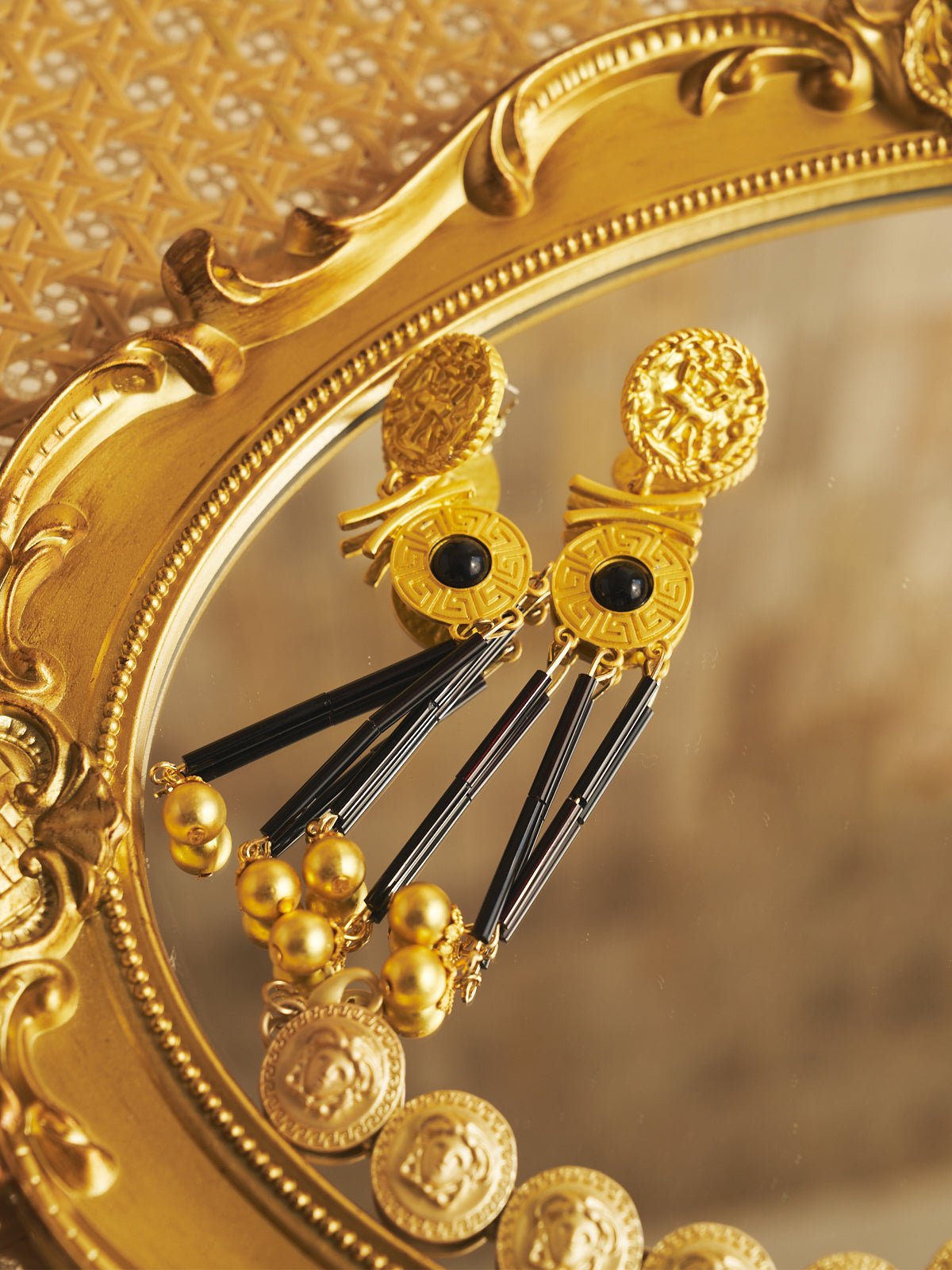 Social Queen’s Gold-Tone Tassel Earrings feature intricate designs and black onyx-inspired beads, making them perfect wedding guest jewelry, elegantly displayed on a gold-framed mirror.