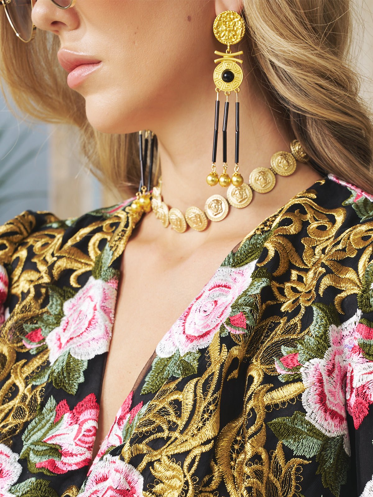 Woman shown from the shoulders up wears a floral embroidered dress and wedding guest jewelry, including a coin necklace and striking Social Queen Gold-Tone Tassel Earrings.