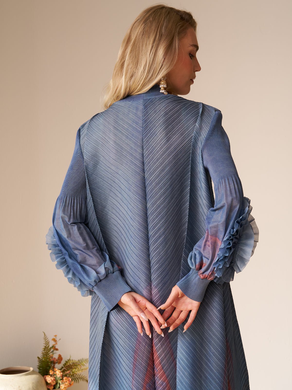 A blonde woman stands with her back to the camera, hands clasped, wearing the Social Queen Gradient Pleated Dress with 3D Floral Sleeves.