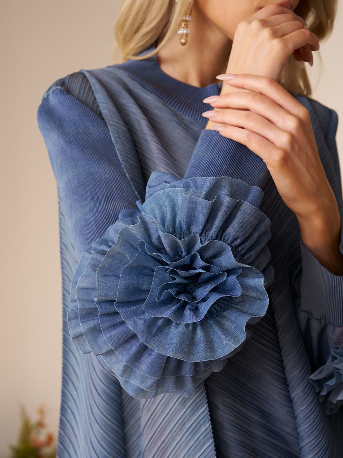 A woman wears the Social Queen Gradient Pleated Dress with 3D Floral Sleeves, featuring textured blue fabric and layered ruffles—a stylish choice for a wedding guest.