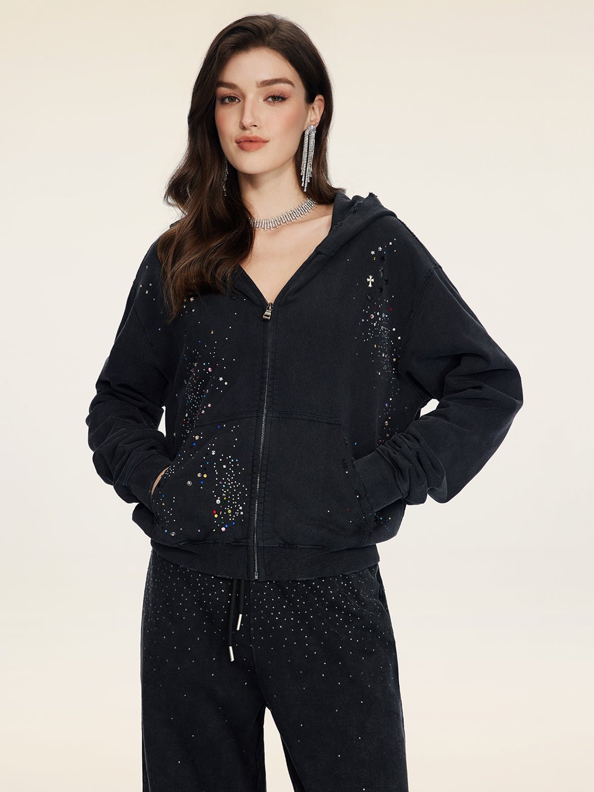 A woman models the Social Queen Hand-Applied Rhinestone Washed Hoodie with matching pants, both in black and embellished with sparkling hand-applied rhinestones, set against a plain light background.