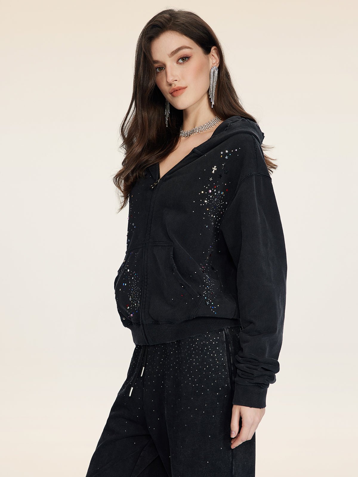 A woman models the Social Queen Hand-Applied Rhinestone Washed Hoodie and matching pants, both adorned with rhinestones, against a simple light background.