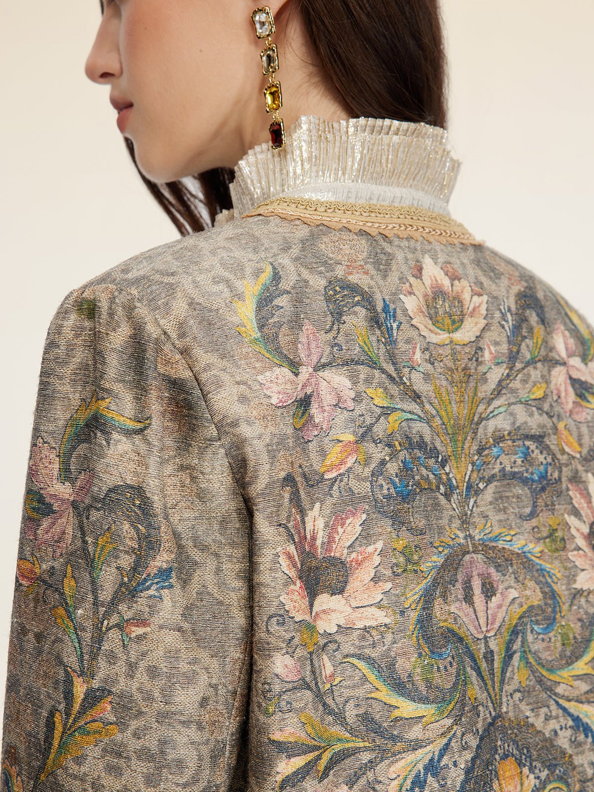 A woman wears the Social Queen Hand-Beaded Printed Jacket with a high pleated collar, paired with a gold and red dangling earring.