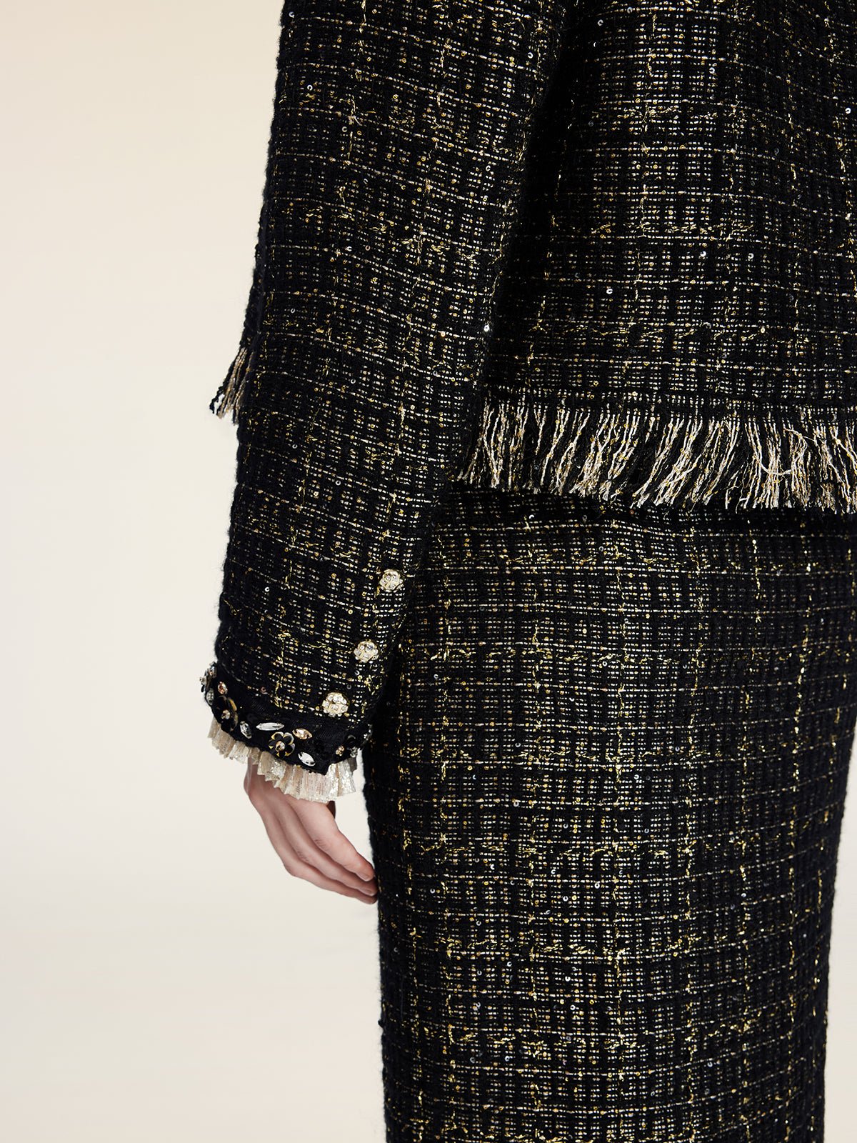 A person wearing the Social Queen Hand-Beaded Tweed Fringe Jacket, featuring black-and-gold tweed, decorative sleeve buttons, fringe accents, and a chic cropped fit.