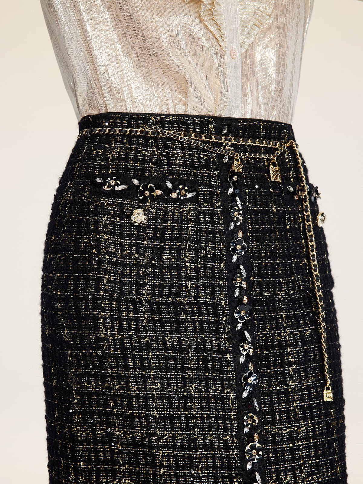 A person wears the Social Queen Hand-Beaded Tweed Fringe Slit Skirt, featuring black-and-gold tweed, decorative chains, floral embellishments, front buttons, and intricate hand-applied beadwork.