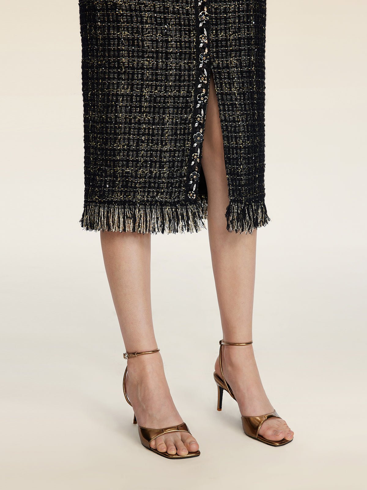 A person wearing Social Queen's Hand-Beaded Tweed Fringe Slit Skirt paired with bronze high-heeled sandals.