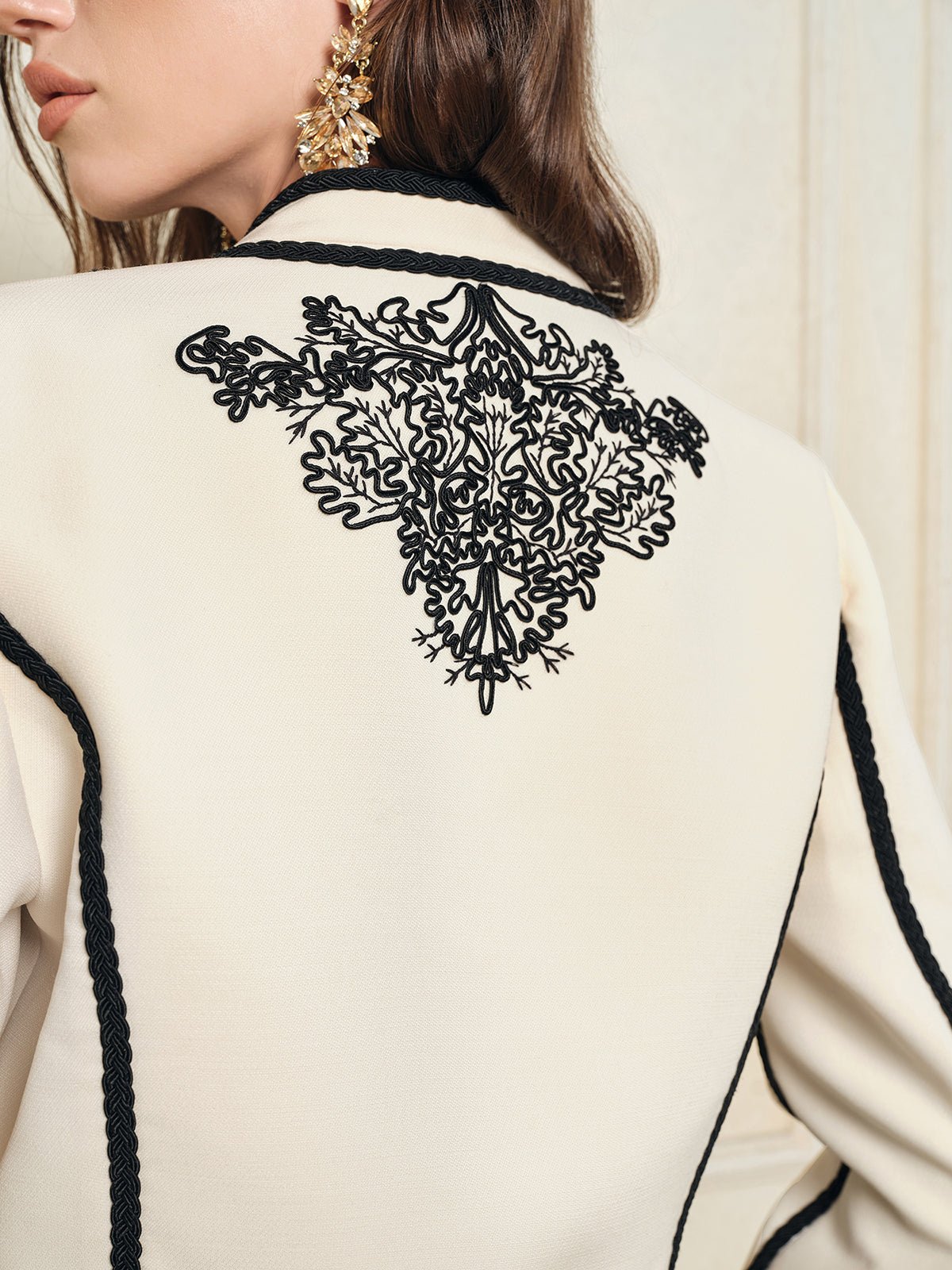 A woman wears the Social Queen Hand-Embroidered Silk-Wool Cropped Tweed Jacket with black lace embroidery and trim, styled with a decorative gold earring.