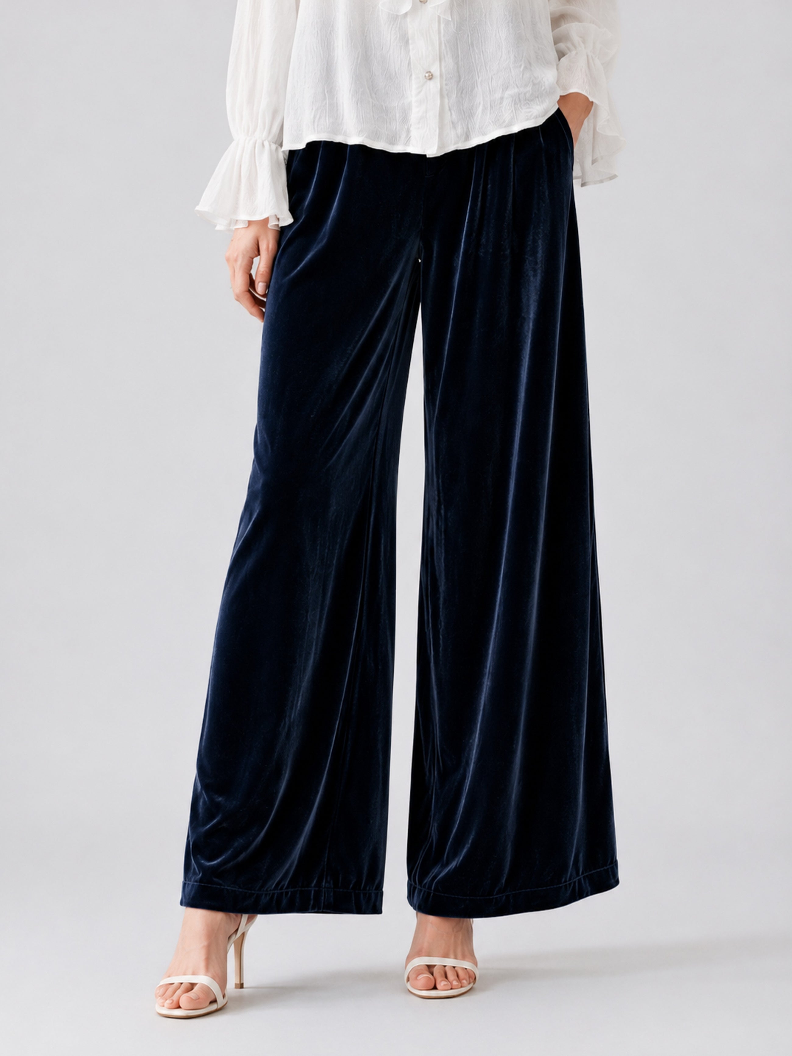 A person wearing the Social Queen Silk Velvet Wide-Leg Pants in navy blue, paired with a white blouse featuring ruffled cuffs and open-toe heels, stands against a plain light background.