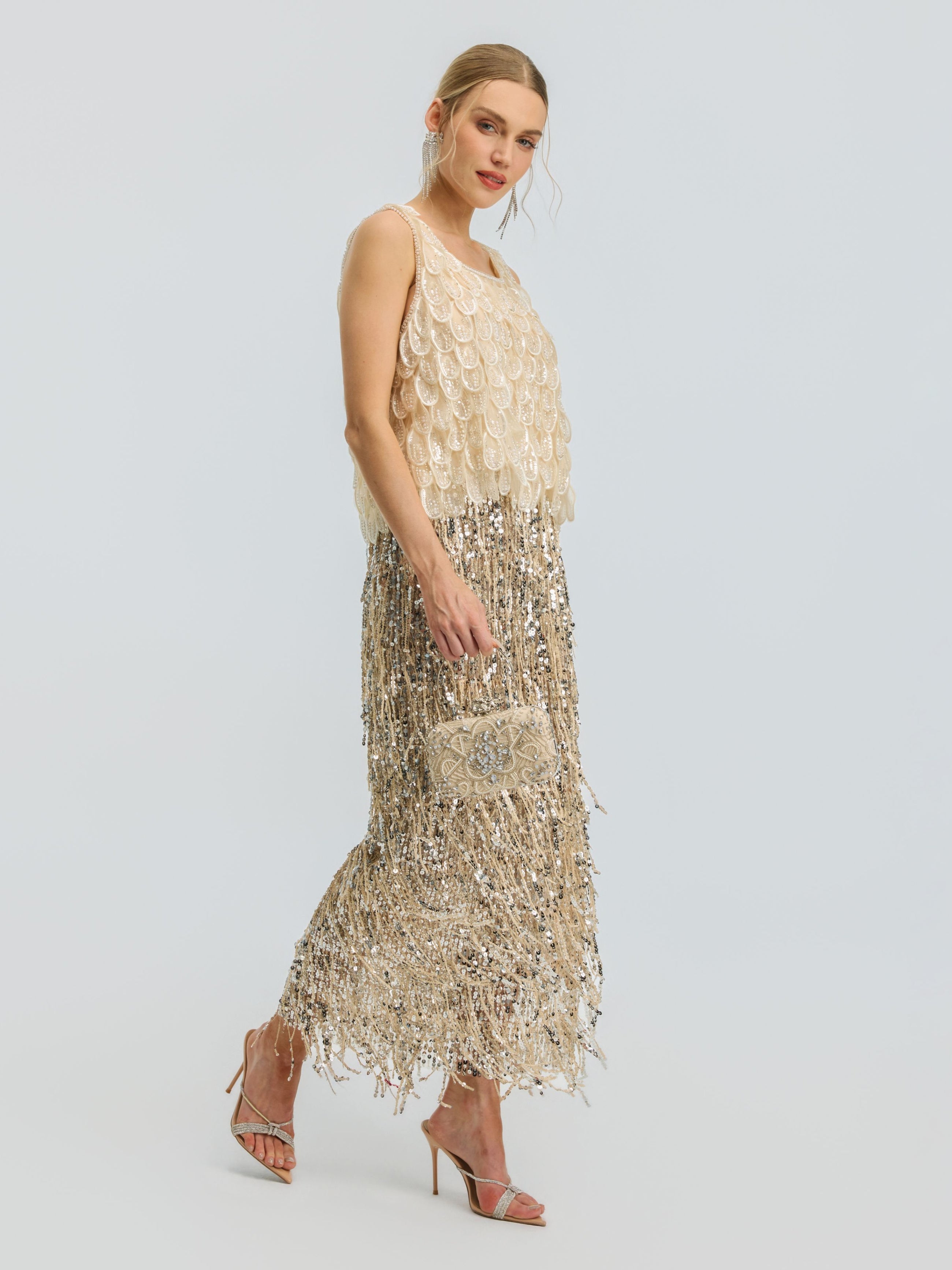 A woman in the Social Queen 3D Leaf Beaded Mesh Top, styled with a small embellished clutch and sandals, stands against a plain light background.