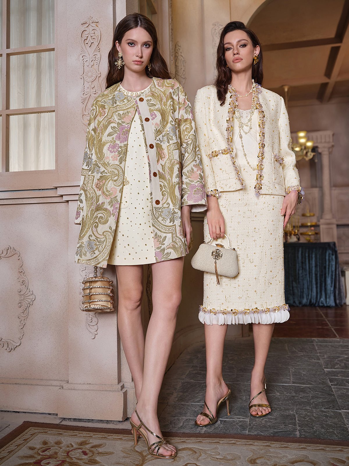 Two women in Social Queen’s Italian Baroque Floral Metallic Jacquard Jackets and heeled sandals pose indoors amid vintage baroque floral decor, radiating sophisticated charm under soft lighting.