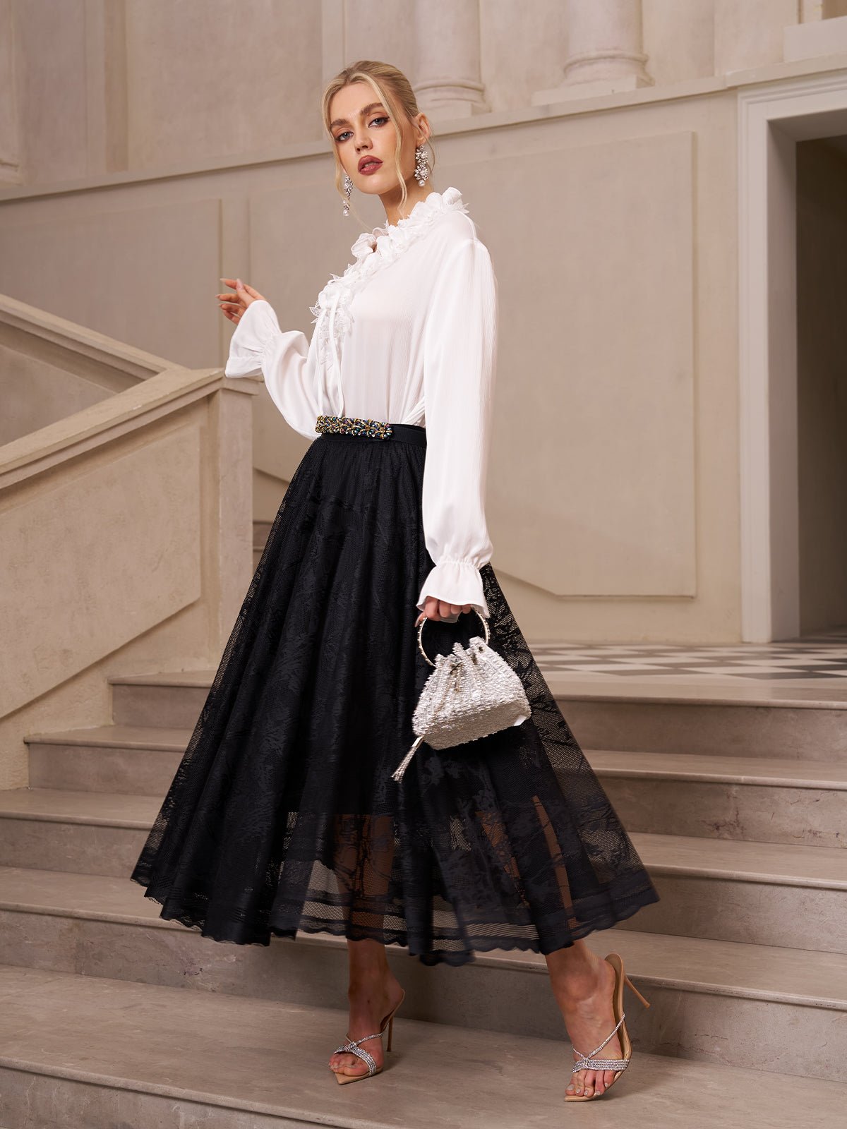 A woman wears the Social Queen Jacquard Lace A-Line Midi Skirt with a white blouse, strappy heels, and a small silver handbag while standing on a staircase.