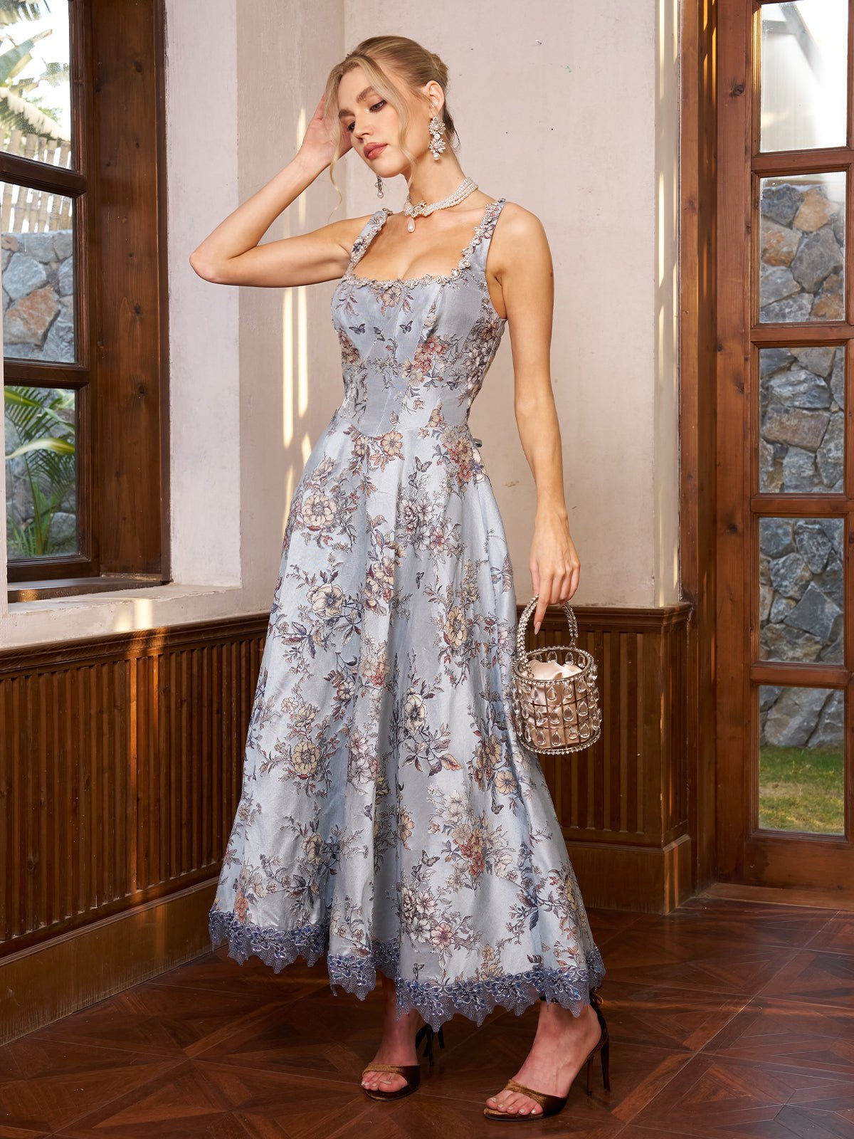 A woman stands indoors by a window wearing the Social Queen Jacquard Strapless Dress with Beaded Detail, earrings, and holding a small beaded handbag.