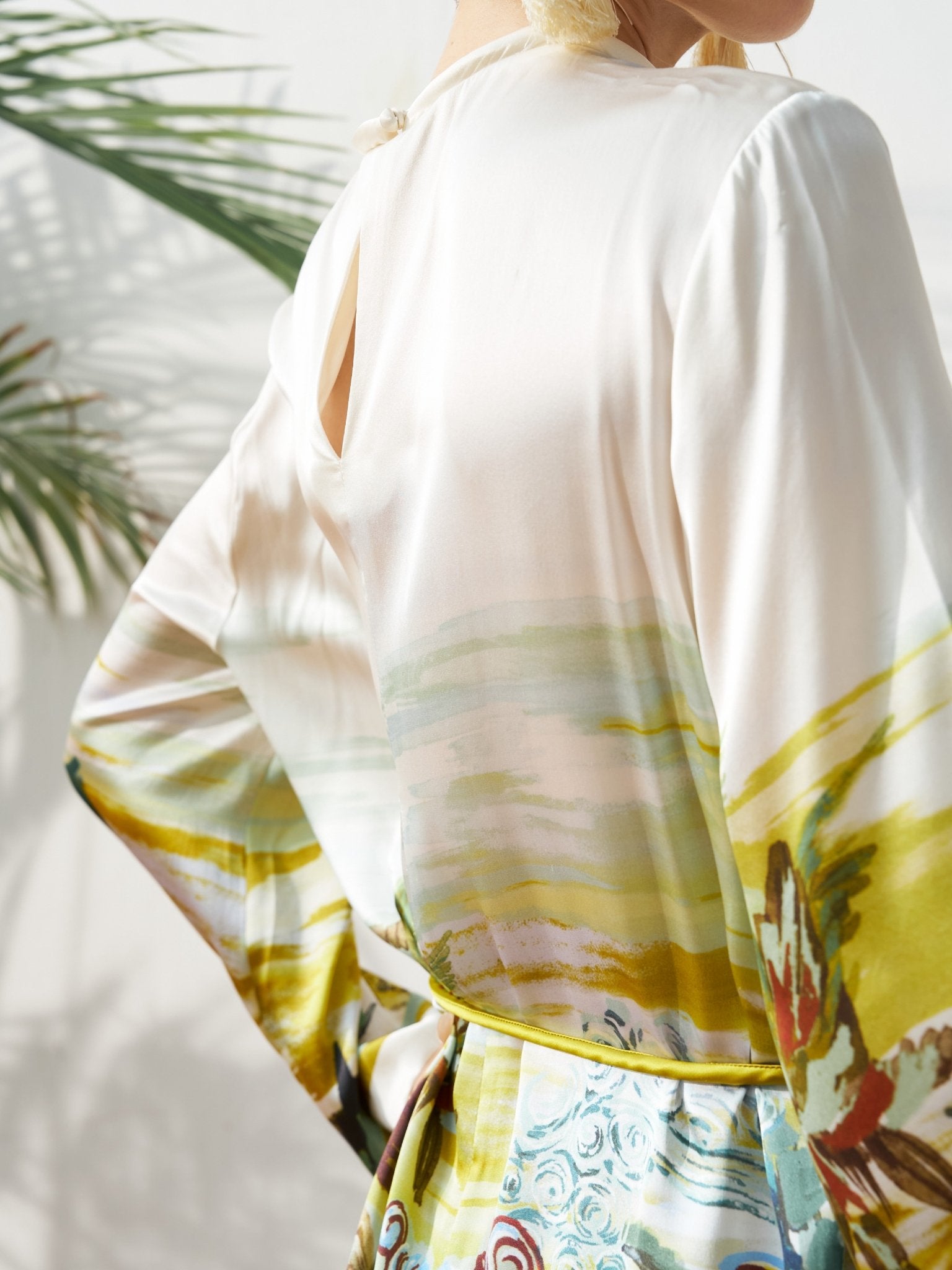 A person wearing the Landscape Print Satin Silk Dress by Social Queen stands near a plant in natural light.