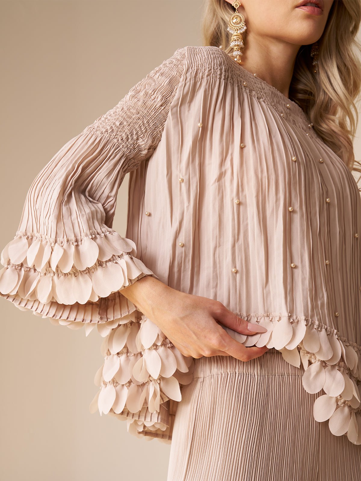 A woman models the Social Queen Layered Petal Beaded Pleated Set—a light pink ensemble featuring textured details and layered petal-like trims on the sleeves and hem, paired with wide-leg pants, perfect as a chic wedding guest outfit.