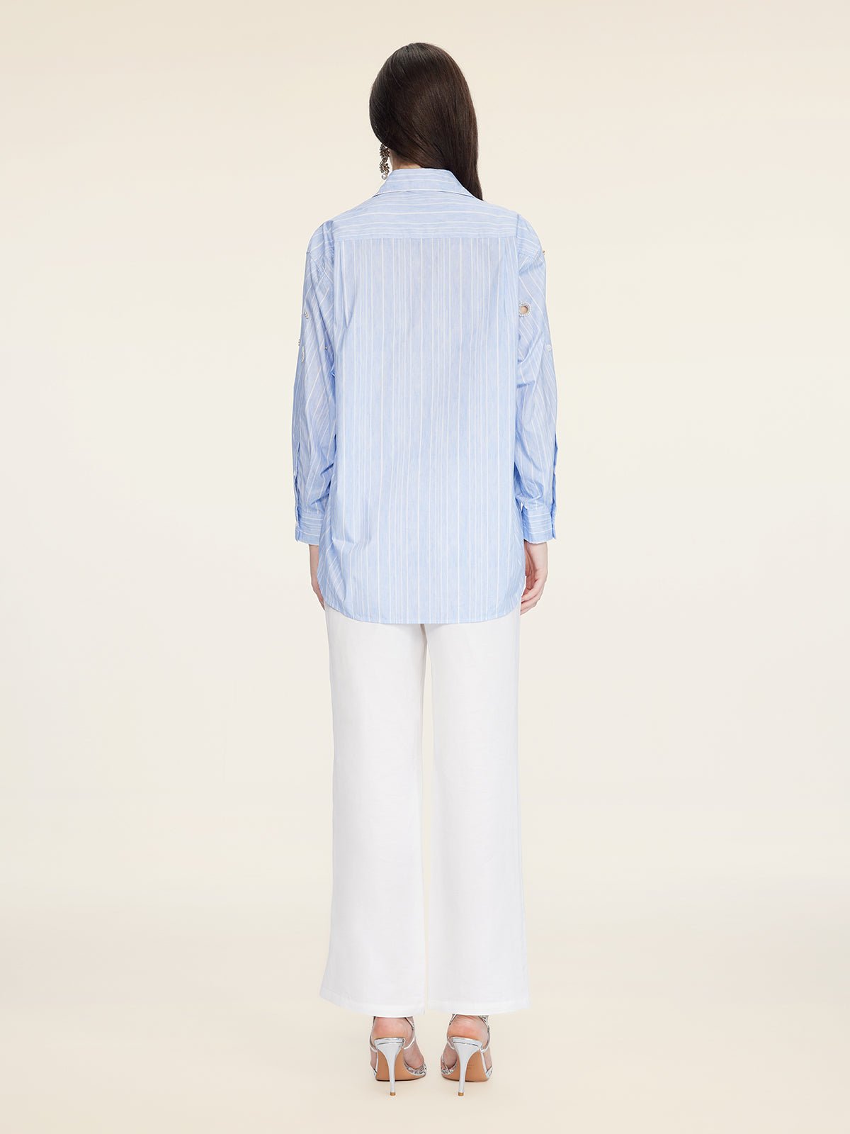 A person stands facing away, wearing the Social Queen Pearl & Beaded Striped Blouse paired with white wide-leg pants and heeled sandals against a plain background.