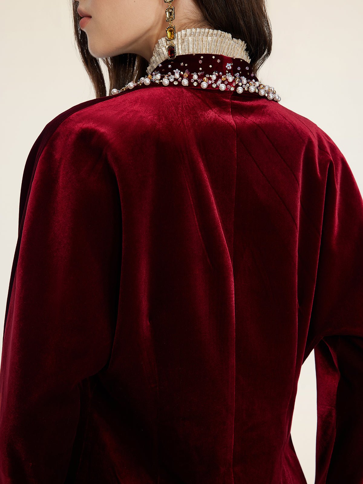A wedding guest is seen from behind in Social Queen's Pearl & Crystal Velvet Blazer, a deep red velvet piece adorned with hand-applied pearls and gemstones on the collar.