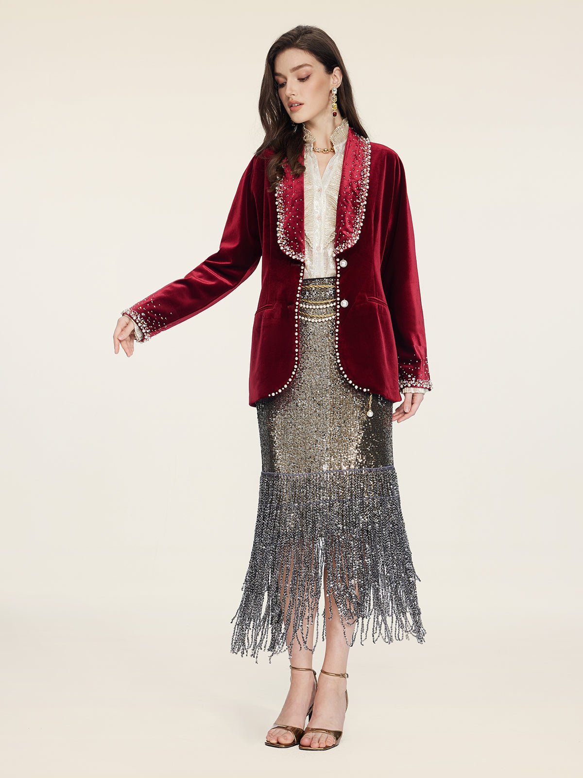 A woman wears the Social Queen Pearl & Crystal Velvet Blazer, styled with a light blouse and silver fringed sequin skirt—an elegant wedding guest look, finished with strappy heels.