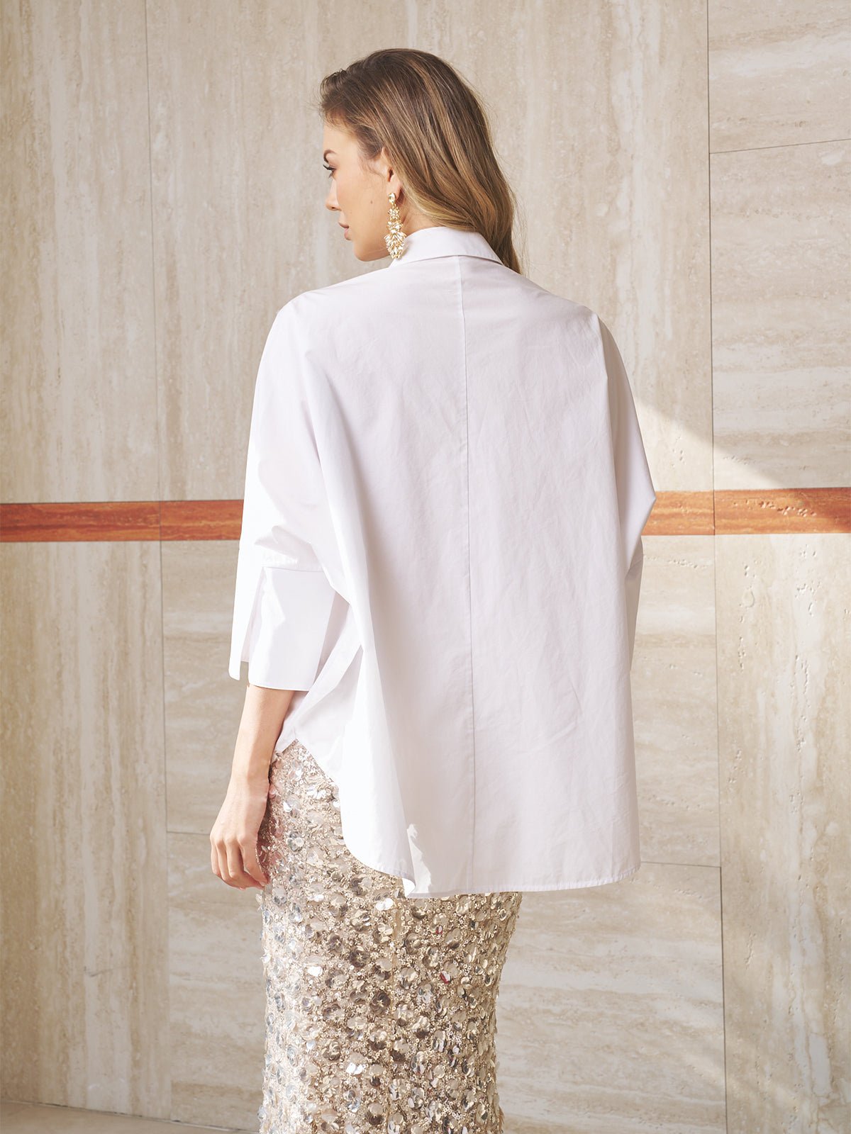 A person stands indoors, facing away, wearing the Social Queen Pearl-Embellished Floral Blouse with a beige tiled wall in the background.