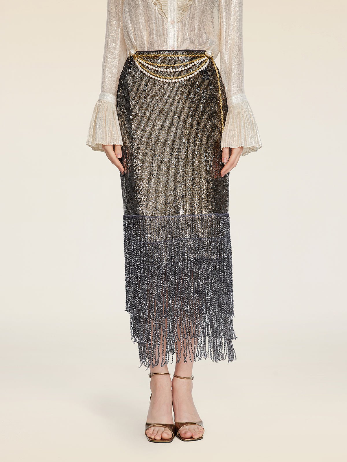 A person wears the Social Queen Pearl-Trim Sequin Fringe Skirt—shimmery, midi length with fringe and chain belt—styled with a sheer long-sleeve blouse and heeled sandals.