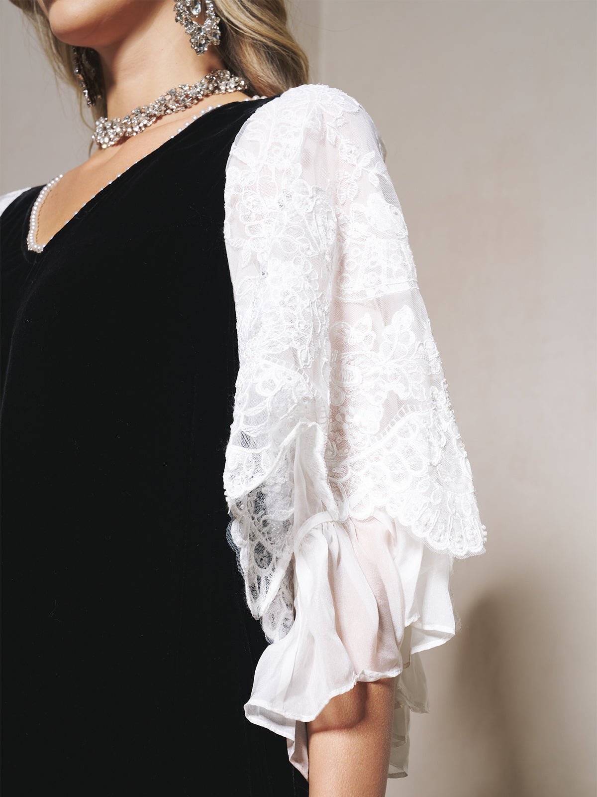 Close-up of a person in the Social Queen Pearl-Trim Silk Velvet Dress with white lace, sheer puff sleeves, and accessorized with a sparkly necklace and earrings.