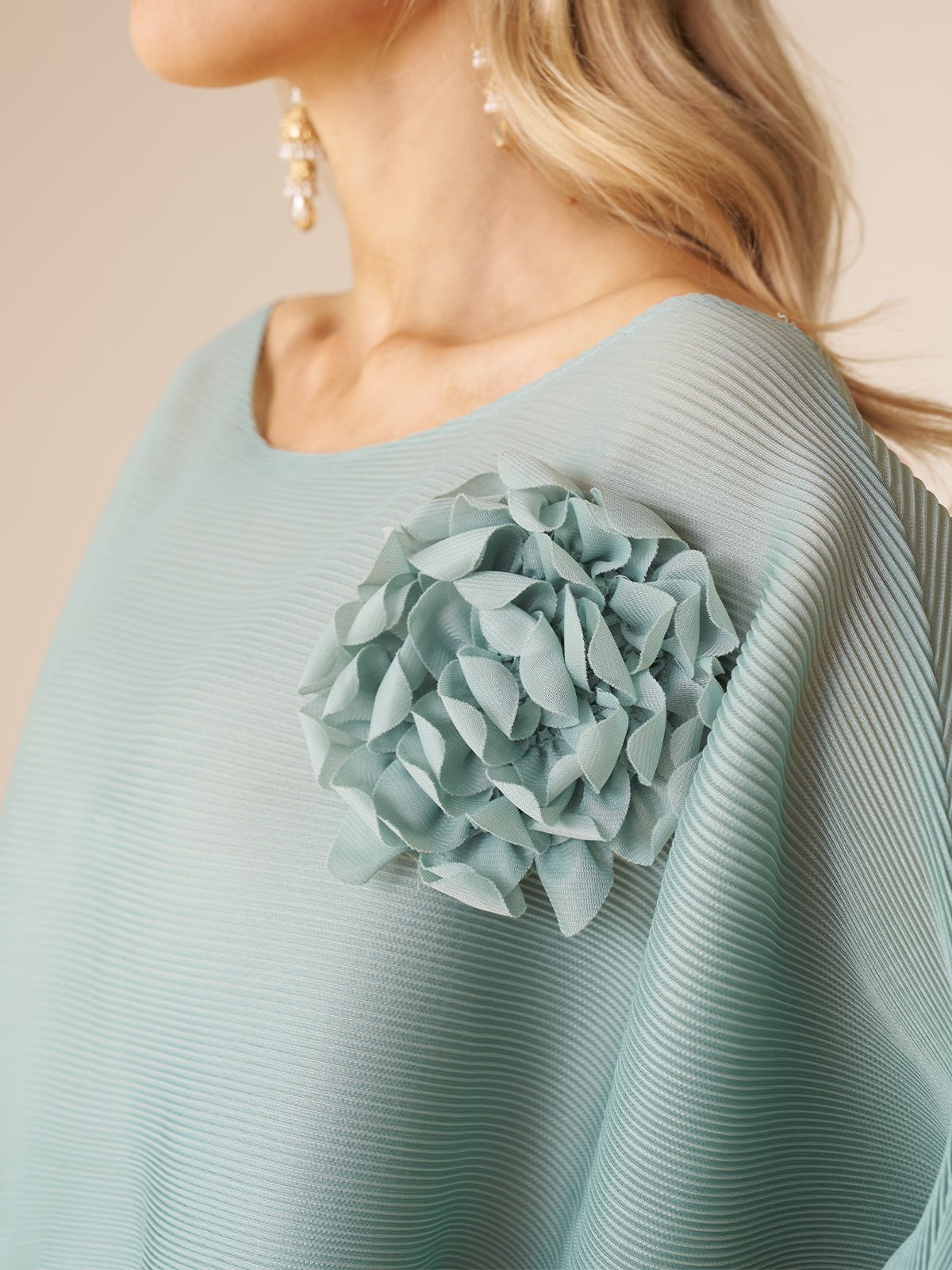 A woman models the Social Queen Pleated Floral Appliqué Set, featuring a textured light blue top with a bold 3D floral shoulder detail, paired with dangling pearl earrings.