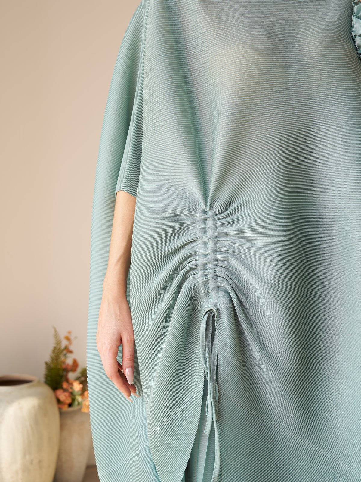 A person wears the Social Queen Pleated Floral Appliqué Set, featuring a loose, light blue, high-waist pleated design with ruched drawstring detail. A vase with flowers appears partially in the background.